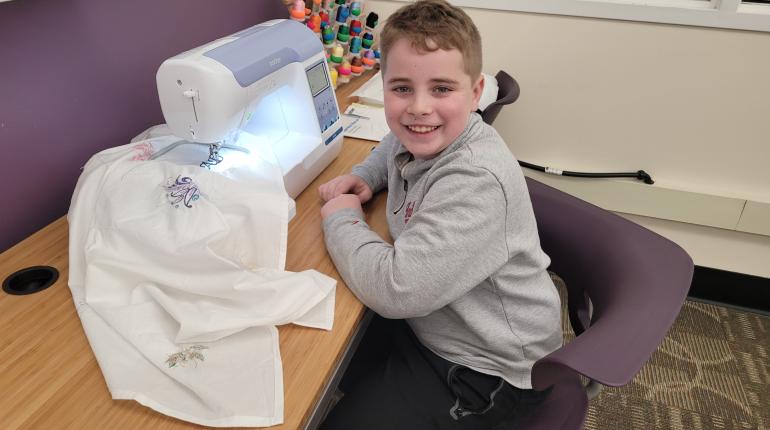 Child smiling up from the digital embroidery machine station.