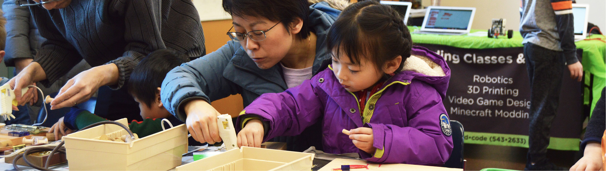 Image of parent and child using glue gun at worktable.