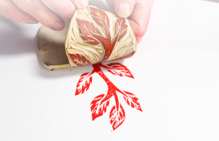 Image of a hand pulling a rubber stamp of a leaf away from paper
