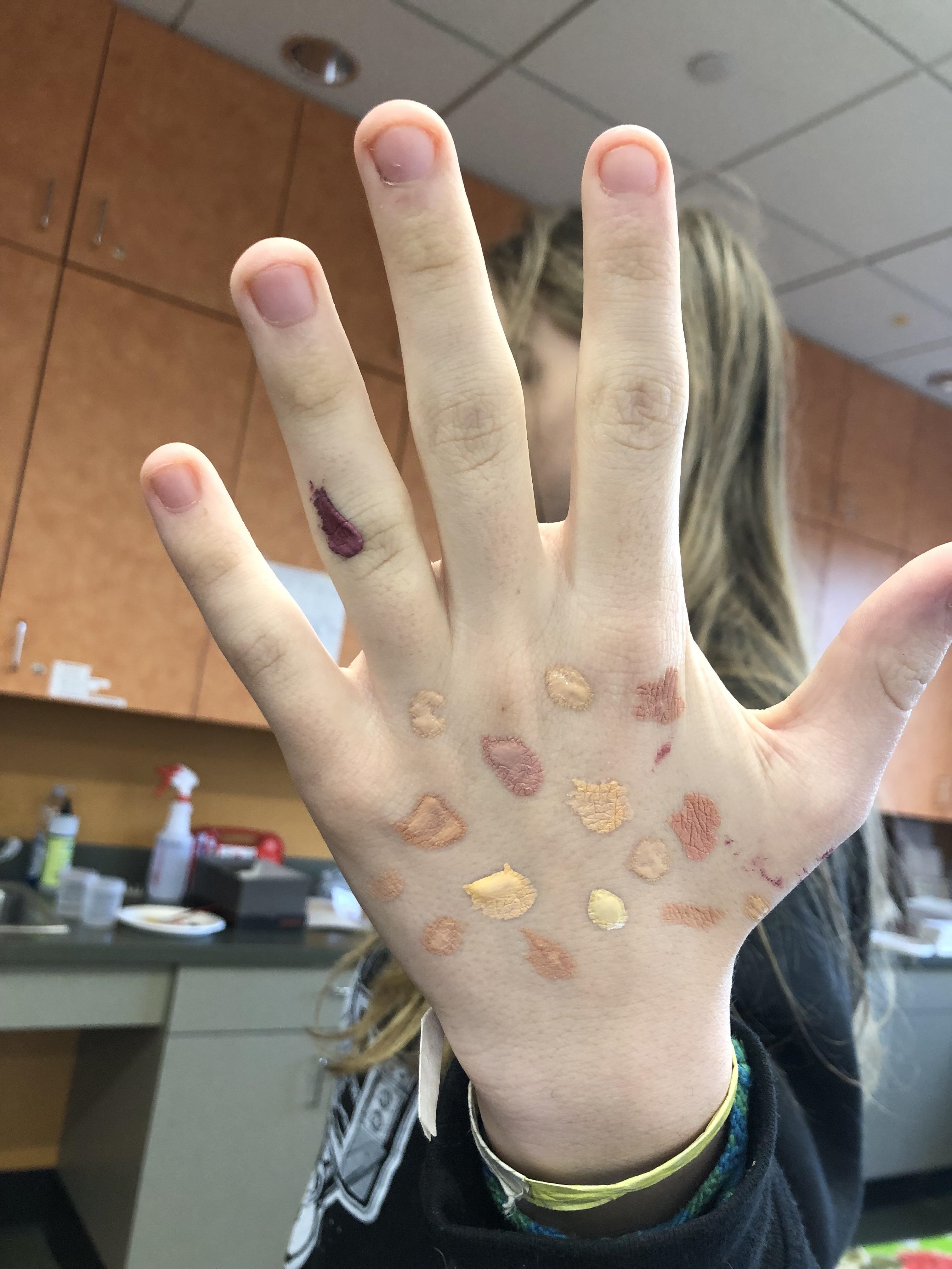 White child's hand with dabs of paint in different skin tones