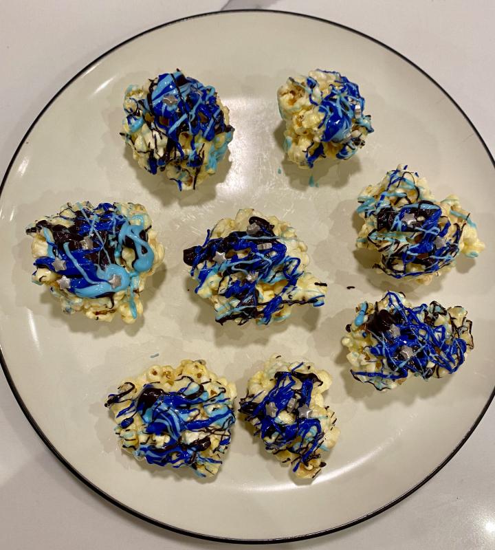 eight blue, purple, and black popcorn balls with star sprinkles on a plate