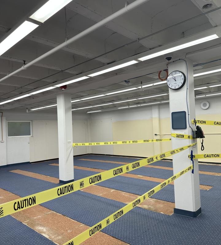Room with caution tape around columns and patchy flooring.